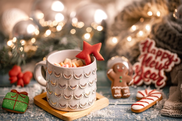 Чашка с горячим напитком, зефир на столе с рождественскими украшениями на фоне с пряниками. Новогодняя концепция.