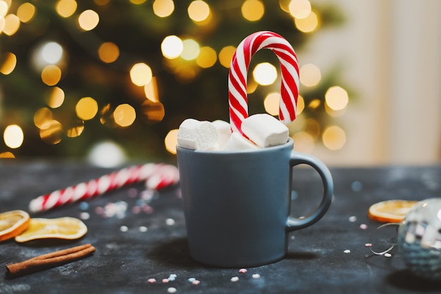 Cup with marshmallows candy cane tangerines by Christmas tree background New Year still life