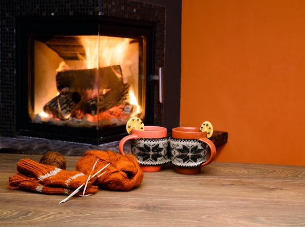 Cup with ornament near fireplace Mug in red knitted mitten standing near fireside Cup of h