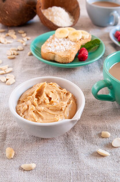 Чашка с арахисовым маслом и коксовыми хлопьями. На заднем плане - бутерброд и чашки с напитками.