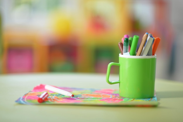 Cup with pencils and colorful drawing on table closeup