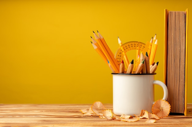 Cup with pencils and pencil shavings on wooden desk against yellow background