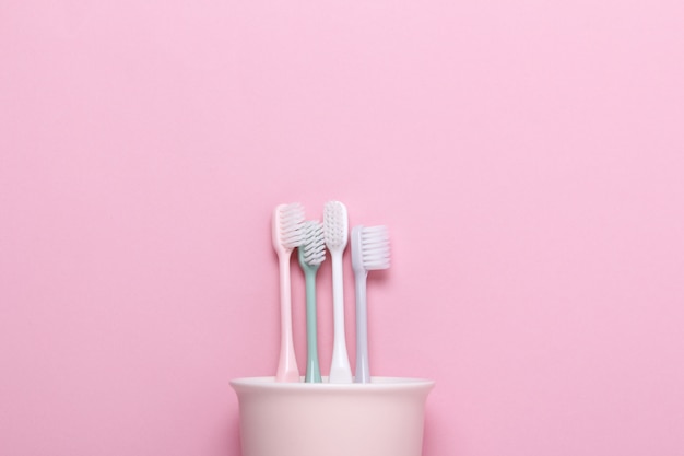 Cup with pink,green,gray and white toothbrushes on pink wall.