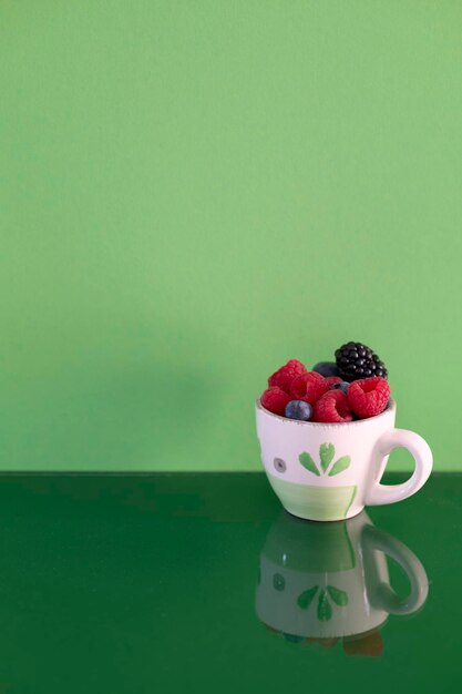 Cup with red fruits on green background