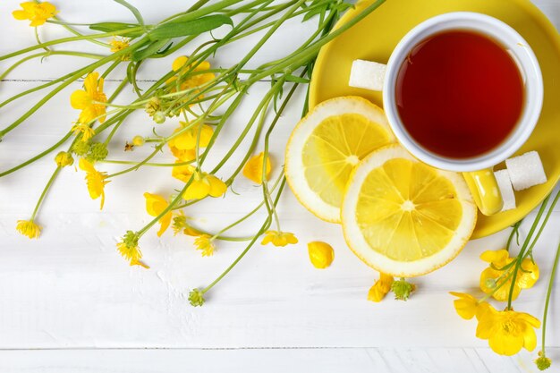 Cup with tea and lemon are on the wooden table.