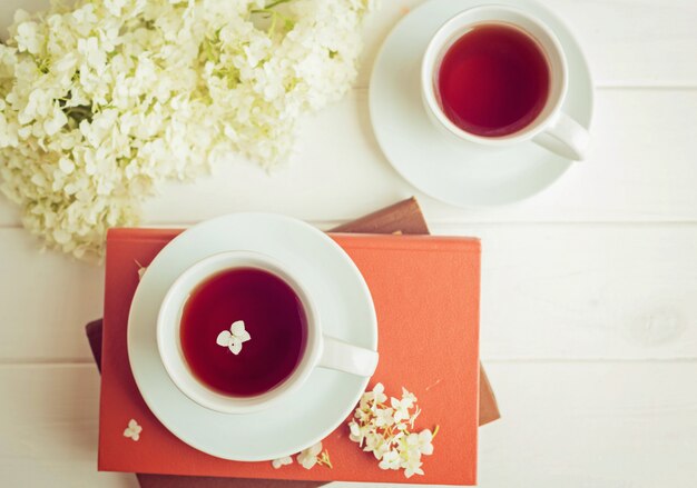 A cup with tea stands on books on a white background. Heart shaped flowers. Morning romantic breakfast.