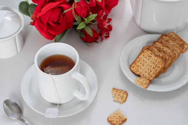 テーブルの上のお茶とカップ 皿の上のクッキー 赤いバラの花束