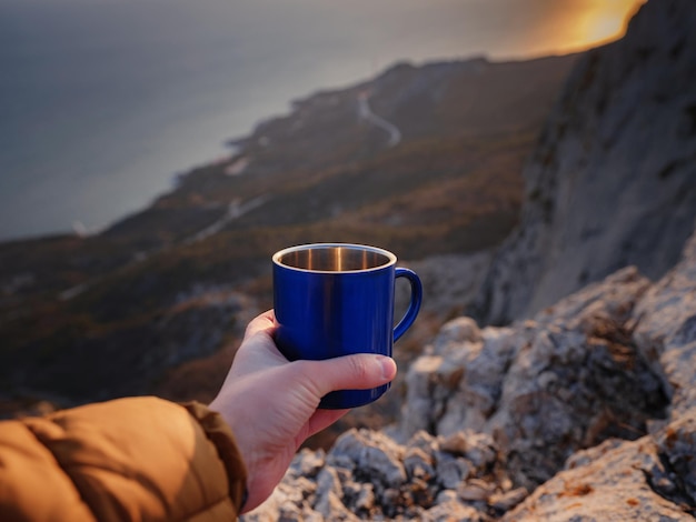 Cup with tea in traveler's hand over out of focus mountains view