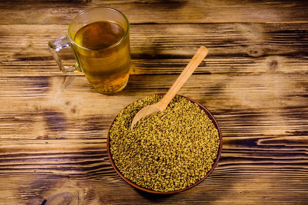 Photo cup of yellow tea methi dana and plate with fenugreek seeds on rustic wooden table