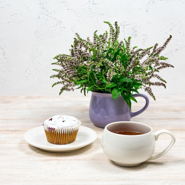 흰색 나무 테이블에 있는 민트 꽃의 배경에 있는 컵케이크와 커피 머그잔 컵케이크가 있는 티 파티