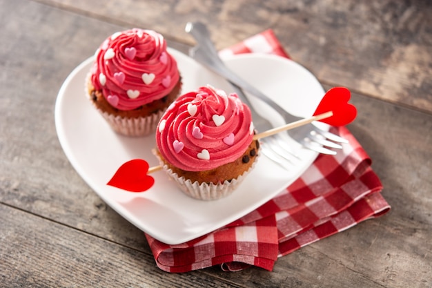 木製のテーブルにバレンタインデーのための砂糖の心とキューピッドの矢で飾られたカップケーキ