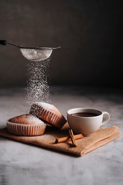 Cupcake on a fiber cloth with a hot chocolate in a mug and a few pieces of cinnamon.