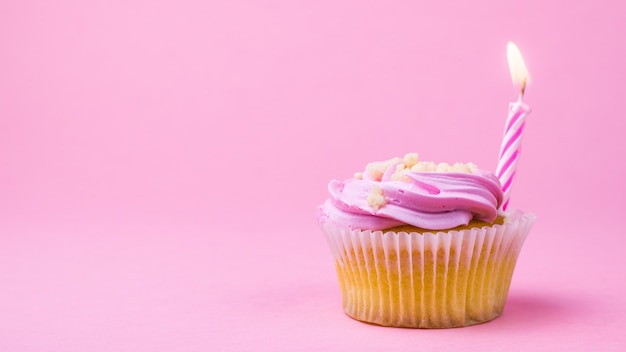 Cupcake met bessenroom en een kaars op een roze ondergrond