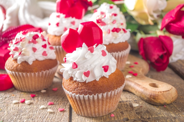 Cupcake met hart voor Valentijnsdag. Valentijnsdag zoet dessert, vanille cupcakes met slagroom vanille en rode suiker hartjes decor voor Valentijnsdag, houten tafel met rozenboeket