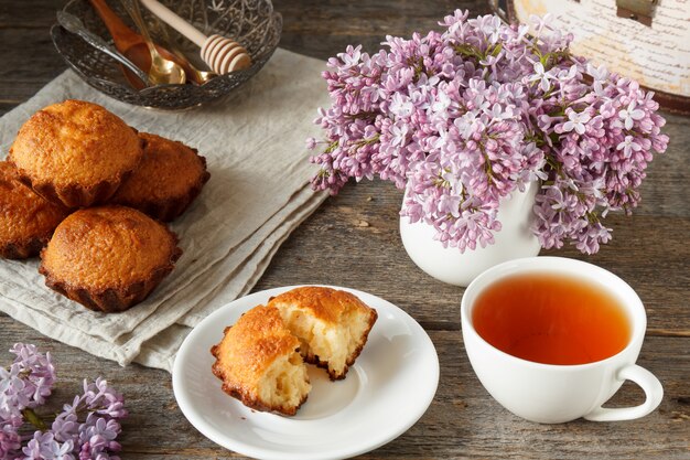 Cupcake on a plate, Cup of tea, a bouquet of lilacs, a few muffins. Wooden background. Still life.