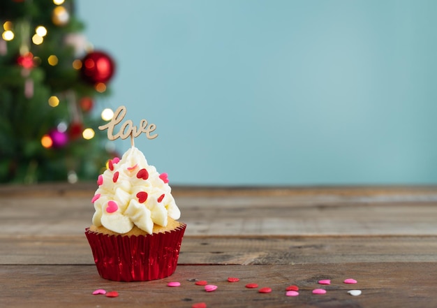 Cupcake versierd op blauwe achtergrond met liefde-teken en onscherpe kerstboom op de achtergrond kopieer de ruimte