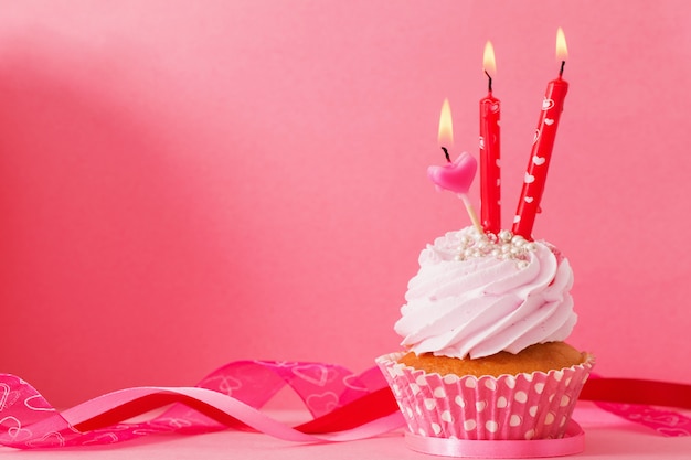 Cupcake with candle on pink background