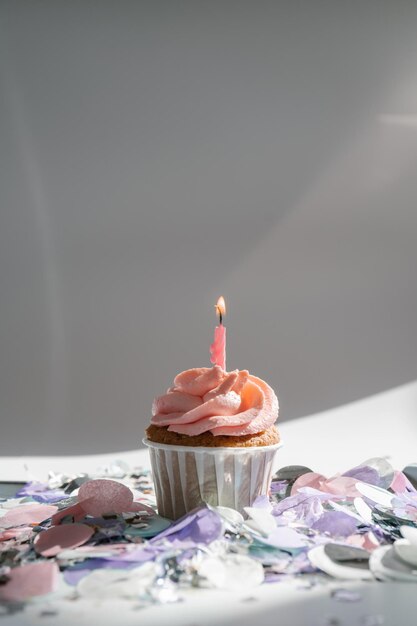 A cupcake with a candle stands on a white background with a\
shadow