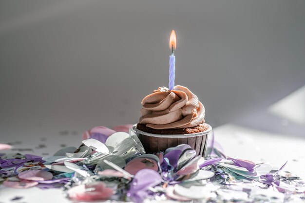 A cupcake with a candle stands on a white background with a
shadow