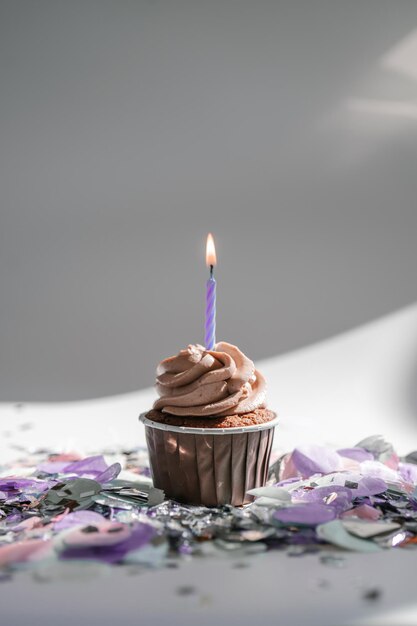 A cupcake with a candle stands on a white background with a
shadow