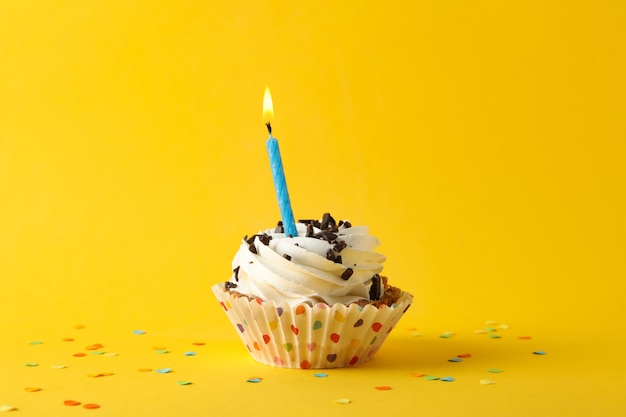 Cupcake with candle on yellow background, space for text