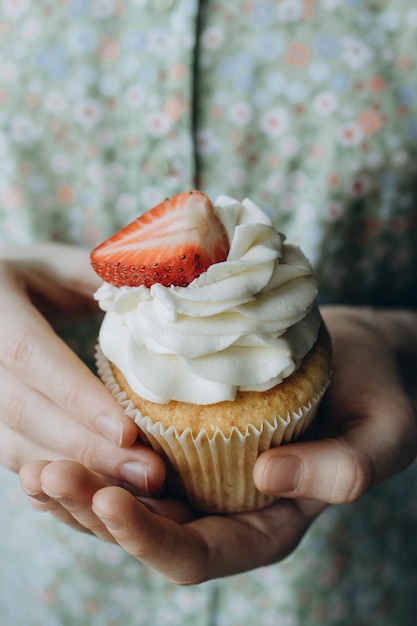 Cupcake with cream decorated with one strawberry in children's hands