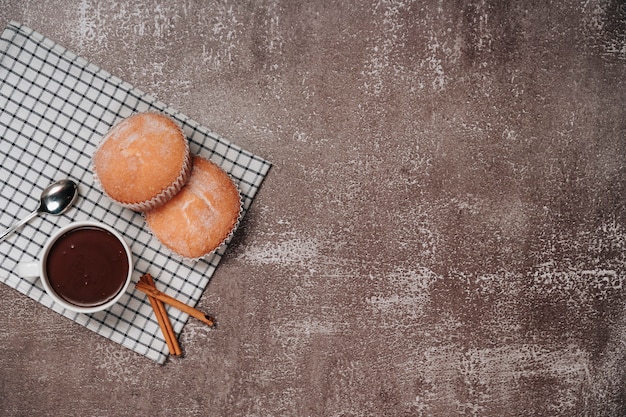 Cupcake with icing sugar on a wooden board with hot chocolate and a few pieces of cinnamon. top view. copy space.