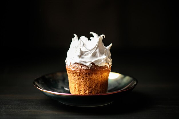 Photo cupcake with meringue cap on a plate on a black background