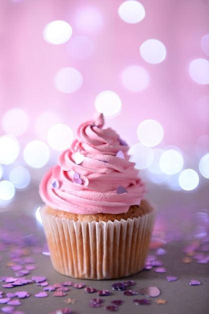 Cupcake with pink cream icing on a glitter background close up