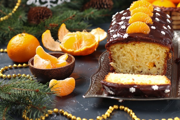 Кекс с мандаринами, покрытый шоколадной глазурью, расположен на новогоднем фоне.