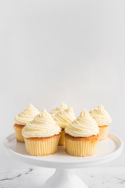 Photo cupcake with whipped cream on cake stand against white backdrop