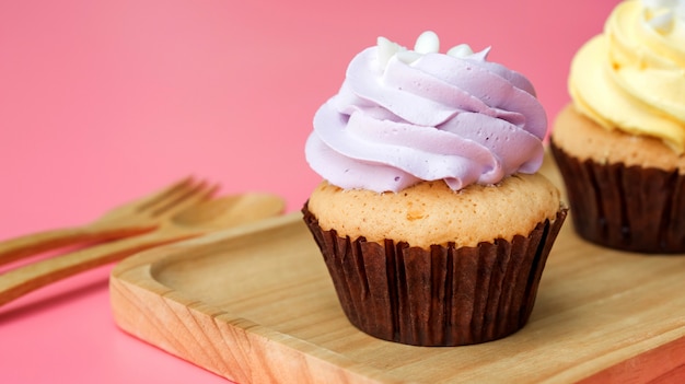 Cupcake su un piatto di legno e sfondo rosa.