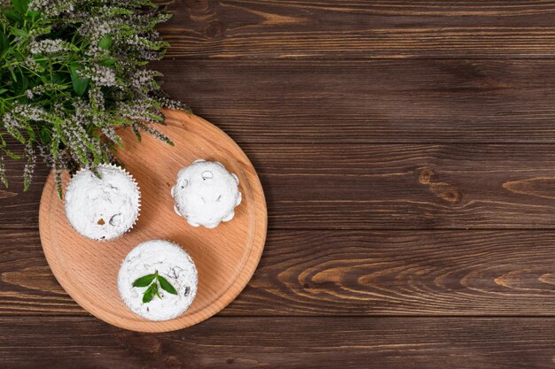 Cupcakes on a background of flowers and mint leaves on a round board on a wooden background Place for gadpis