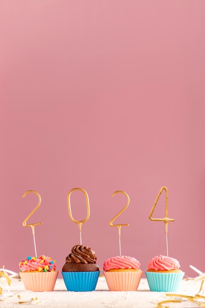 Photo cupcakes or muffins with buttercream frosting decorated with gold 2024 numbers on pink background vertical frame