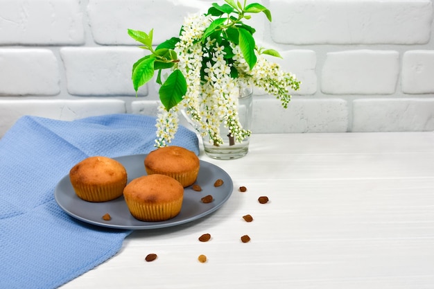 Cupcakes with a bouquet of white flowers Cupcakes on a plate with a blue tablecloth and a bouquet of flowers on a white wooden table Place for an inscription