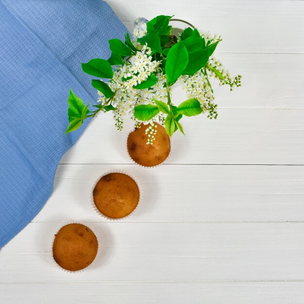 cupcakes with a bouquet of white flowers three cupcakes on a diagonal table with a blue tablecloth and a bouquet of flowers on a white wooden table