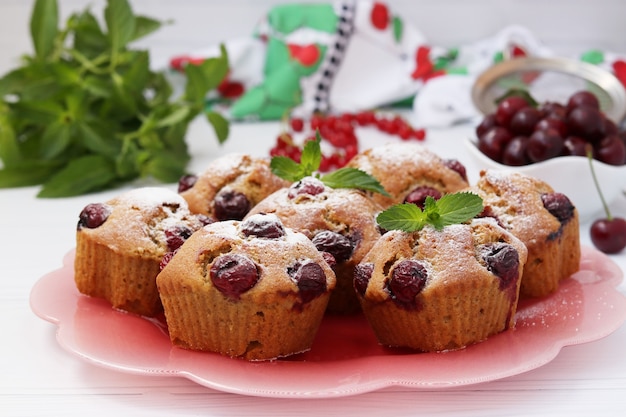 Cupcakes with cherries are located on a plate on a white