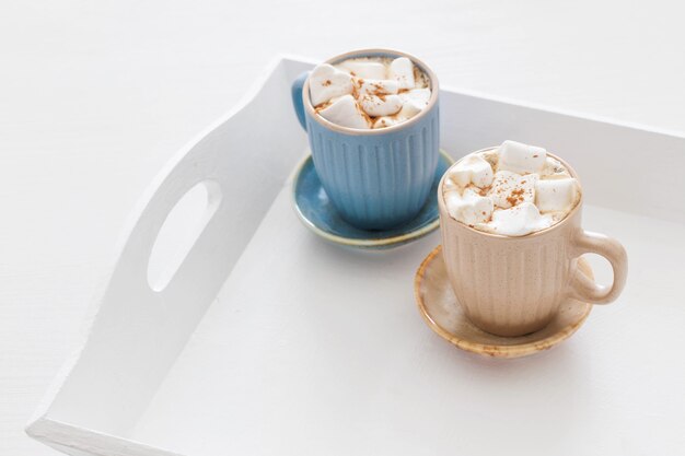 Cups of cacao with marshmallows on white wooden tray