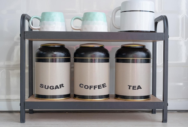 Cups of coffee, tea and sugar cans on the kitchen counter.