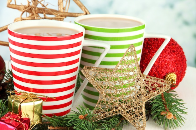 Чашки горячего какао с рождественскими украшениями на столе на ярком фоне