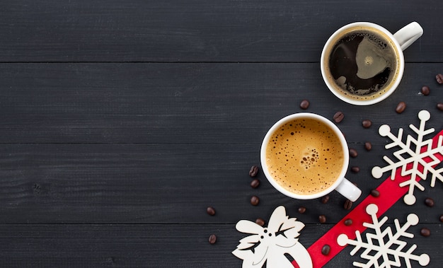 Cups of hot coffee on black wooden surface in Christmas time