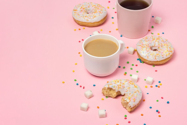 Cups met koffie of thee, verse smakelijke zoete donuts op een roze achtergrond. Fast-food concept, bakkerij, ontbijt, snoep, koffieshop. Plat lag, bovenaanzicht, kopie ruimte.