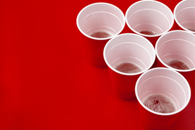 Cups and plastic ball on red background. Beer pong game