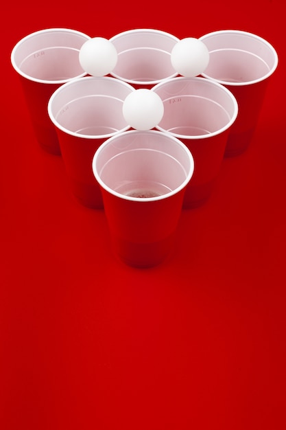 Tazze e palla di plastica su fondo rosso. gioco del beer pong