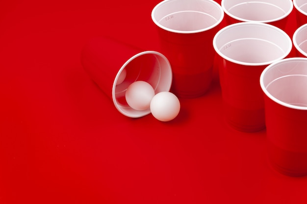 カップと赤の背景にプラスチックボール。ビールポンゲーム