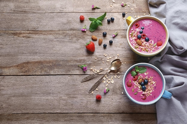 Cups with acai smoothie and berries on wooden background