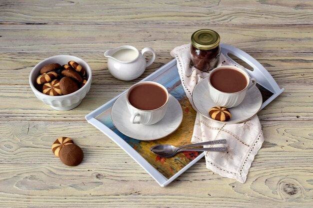 Чашки с горячим какао и печеньем в миске на деревянном столе крупным планом