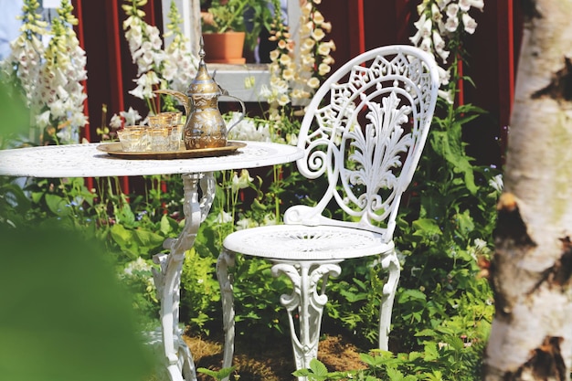 Photo cups with teapot on table by empty chair in yard