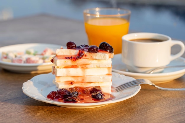 Ricotta con marmellata di ciliegie rosse, succo d'arancia e tazza di caffè sul tavolo concetto di colazione