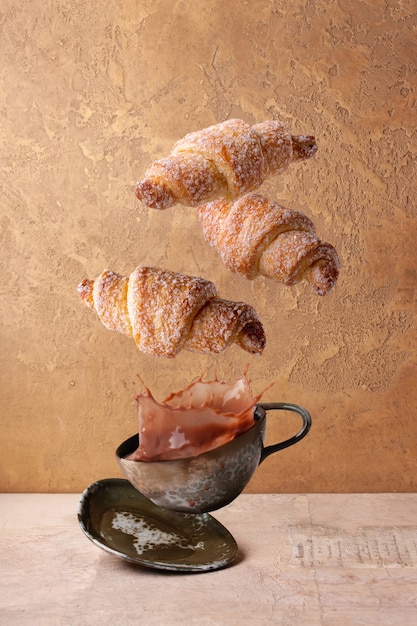 Curd mini croissants fly over a cup of coffee